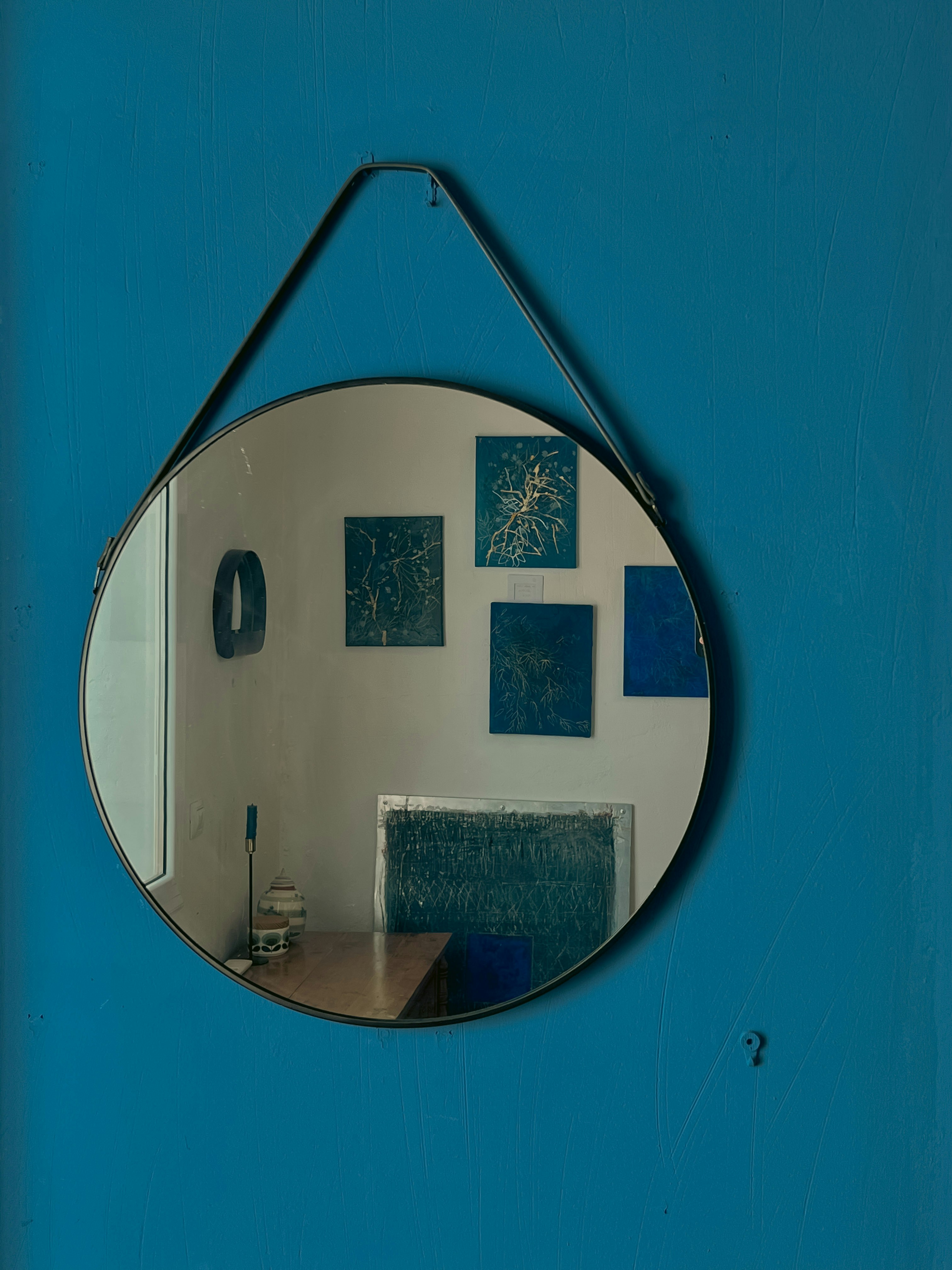 Round mirror reflecting artwork on blue wall